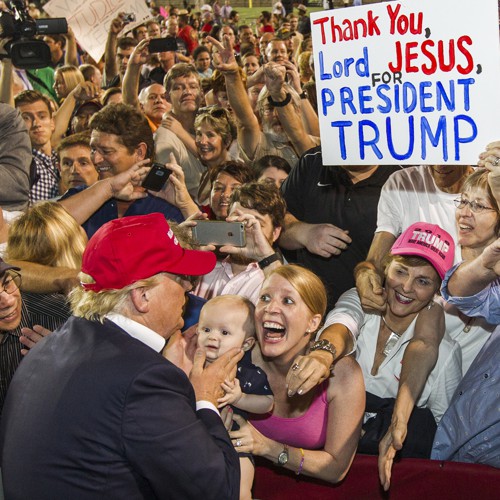 photo of rallygoers at a Trump campaign event, where one attendee held up a sign saying, "Thank You Jesus for Donald Trump" and another woman in religious ecstasy, holds up her toddler for Trump to bless it.